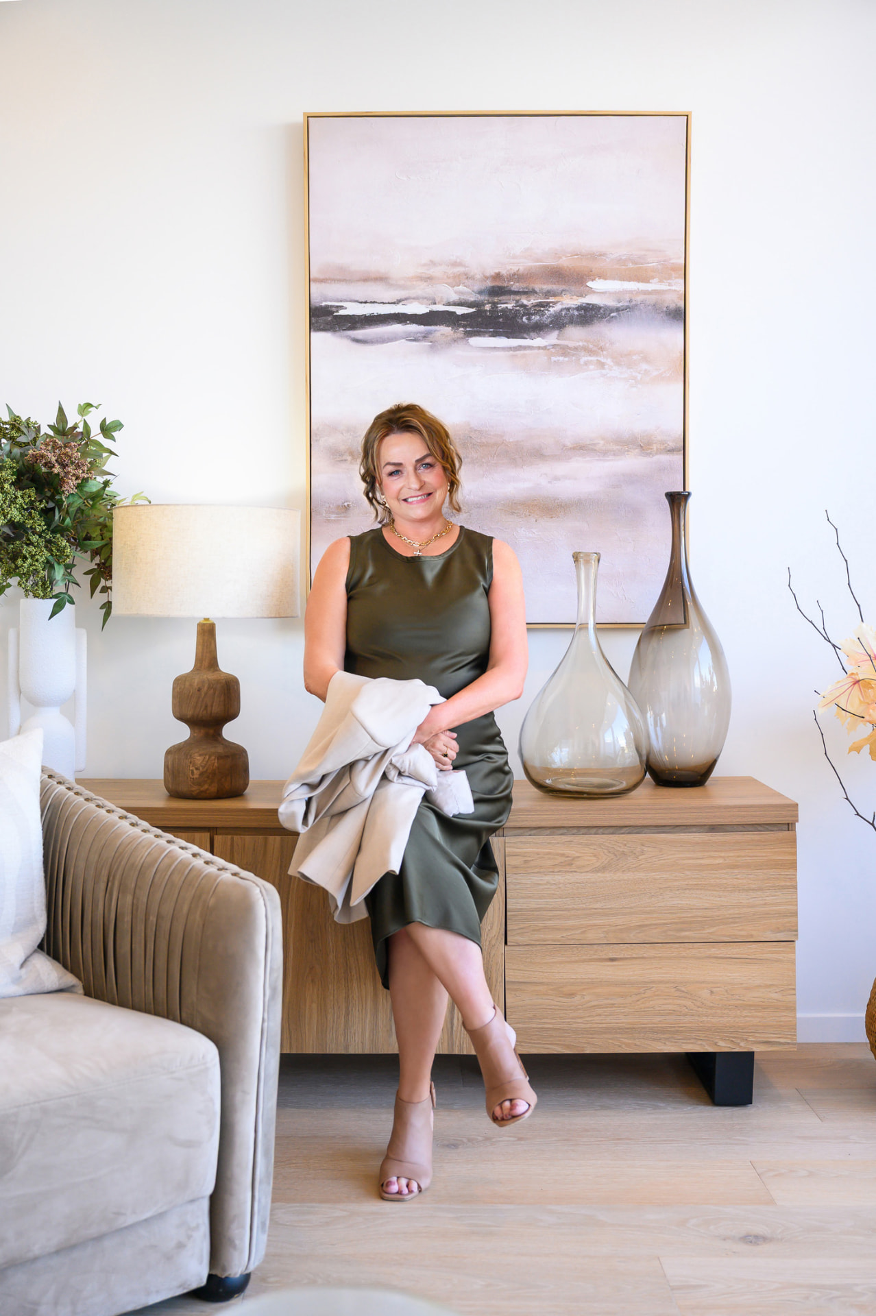 Sherryl Hanlin seated in a styled living room with neutral tones and soft furnishings